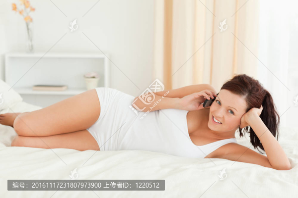 迷人的女人打電話，在她的床上望著鏡頭