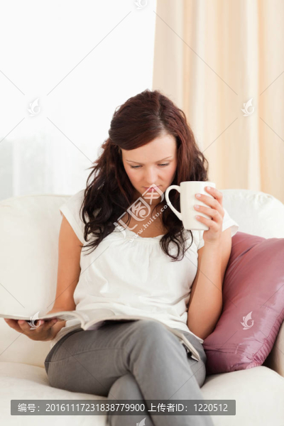 年輕女子一邊看雜志一邊捧著杯子