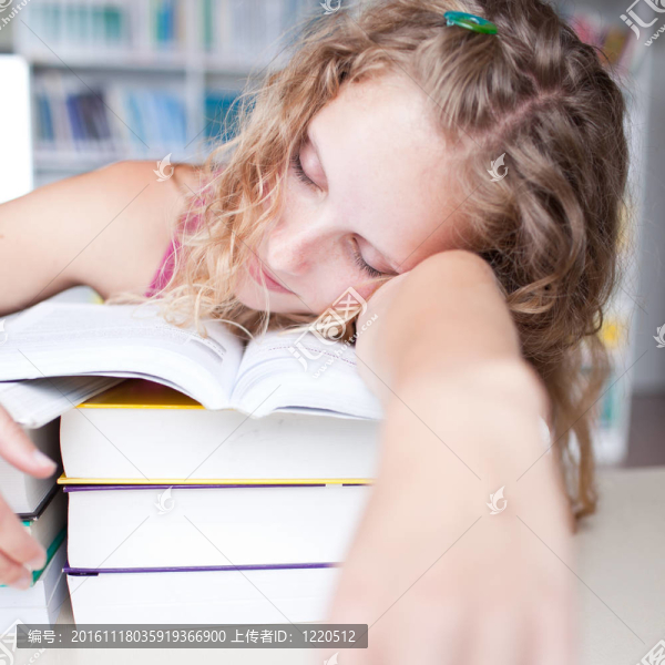 漂亮的女的疲倦/困大學(xué)生午睡在圖書館（淺景深；顏色色調(diào)的圖像）