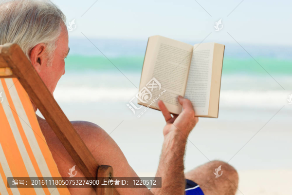高級男子在海灘上讀一本書