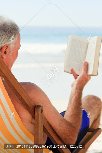 高級男子在海灘上讀一本書