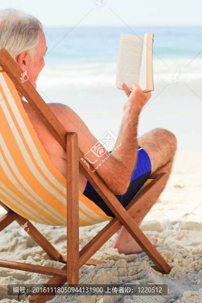 高級男子在海灘上讀一本書