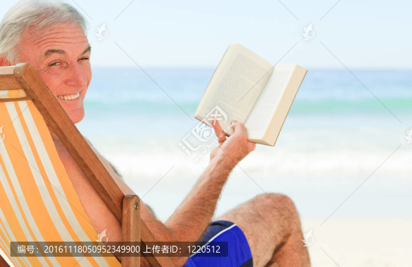高級男子在海灘上讀一本書