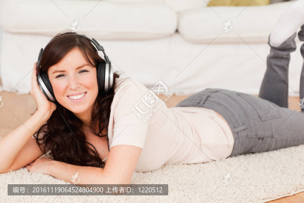 美麗的黑發(fā)女人使用耳機(jī)而趴在客廳的地毯-匯圖網(wǎng) www.fosd68.com 美麗的黑發(fā)女人使用耳機(jī)而趴在客廳的地毯