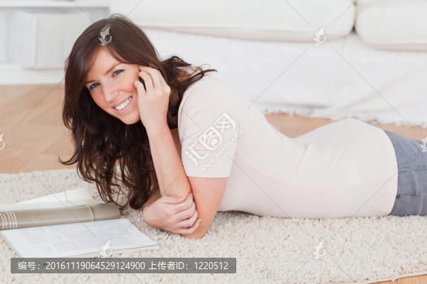 年輕漂亮的女人躺在客廳的地毯上看雜志