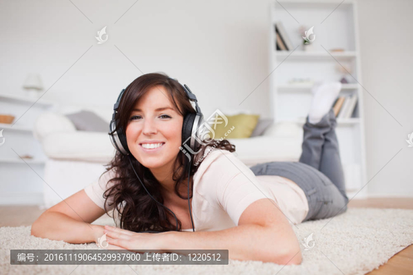 漂亮的黑發(fā)女性使用耳機(jī)而趴在客廳的地毯