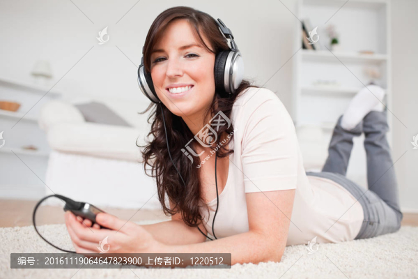 美麗的黑發(fā)女人的MP3播放器聽音樂(lè)，趴在客廳的地毯