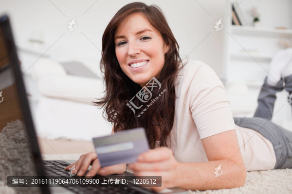 年輕漂亮的女性在客廳躺在地毯上用信用卡付款