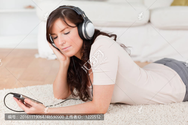 迷人的黑發(fā)女聽音樂與她的MP3播放器，趴在客廳的地毯