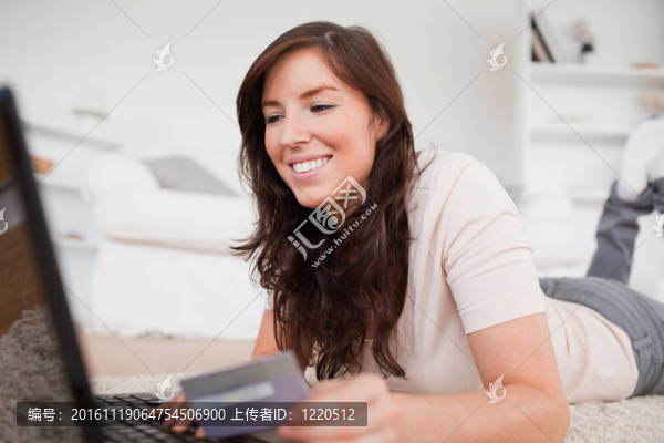 年輕迷人的女性在客廳躺在地毯上用信用卡付款
