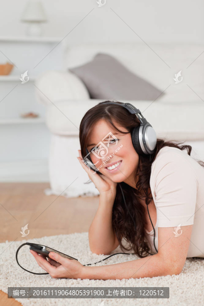 美麗的黑發(fā)女聽音樂與她的MP3播放器，趴在客廳的地毯