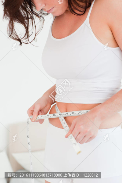 迷人的黑發(fā)女人測(cè)量她的腹部，用卷尺在她臥室的站