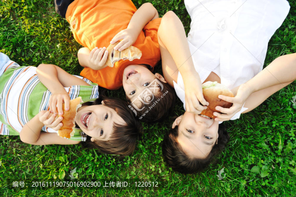 三個(gè)孩子躺在草地上的草地上，吃三明治和微笑；健康的食物；良好的友誼和愛和幸福無(wú)限制：：）