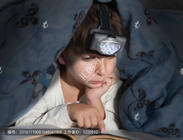 男孩用手電筒在書下看書