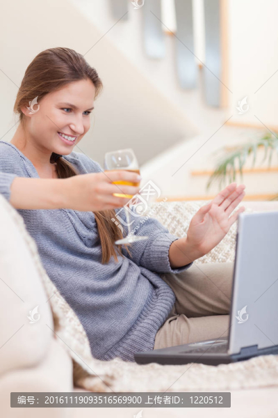 一個女人在客廳里的視頻會議上喝一杯白葡萄酒的畫像