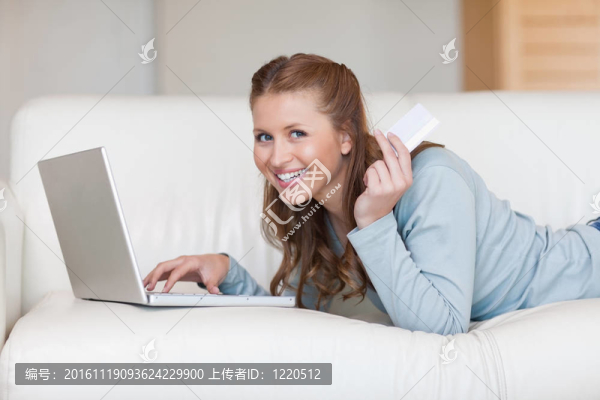 微笑的女人在沙發(fā)上用她的信用卡在線