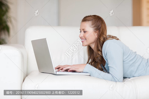 在沙發(fā)上愉快的微笑的女人在她的筆記本上打字