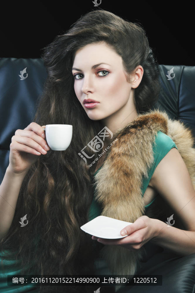 年輕優(yōu)雅的女士躺在沙發(fā)上，喝著一小杯咖啡。穿著綠色的衣服。她看著鏡頭，右手拿著杯子，左手拿著茶托.。