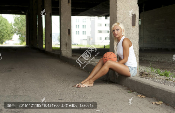 漂亮的金發(fā)女孩坐在街上打籃球