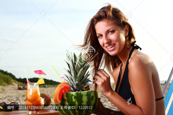 美麗的女孩drinkig水果雞尾酒在沙灘上