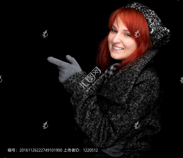 指著年輕漂亮的紅發(fā)女人戴著溫暖的冬帽和外套；黑色背景