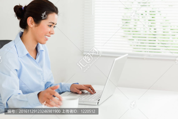 迷人的女人放松與她的筆記本電腦，同時(shí)享受一杯咖啡在辦公室