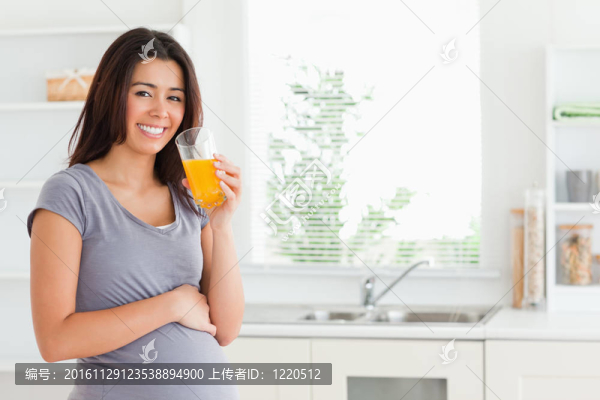 美麗的孕婦站在廚房里喝著一杯橙汁