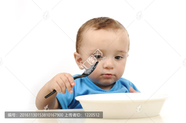 可愛的可愛的一歲的嬰兒在桌子上吃綠色的眼睛；勺子和盤子