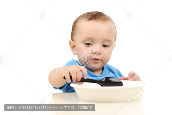 可愛的可愛的一歲的嬰兒在桌子上吃綠色的眼睛；勺子和盤子