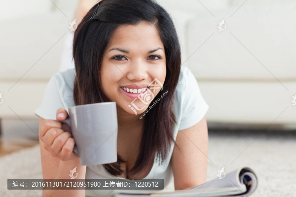 微笑的女人在地板上拿著一個杯子和一本雜志