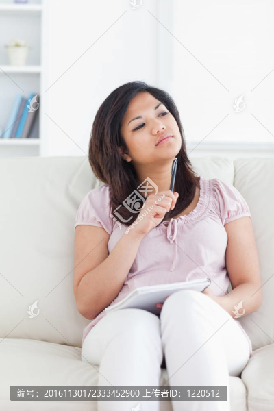 女人坐在沙發(fā)上，拿著一支鋼筆和一個(gè)