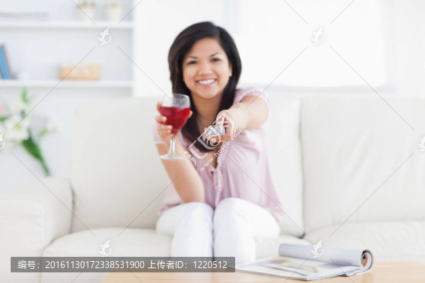 女人坐在白色的沙發(fā)上，手里拿著一杯紅酒