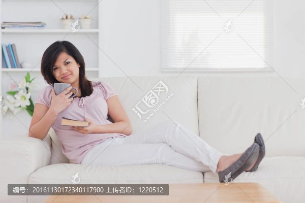 女人坐在沙發(fā)上，手里拿著一個杯子和一本書