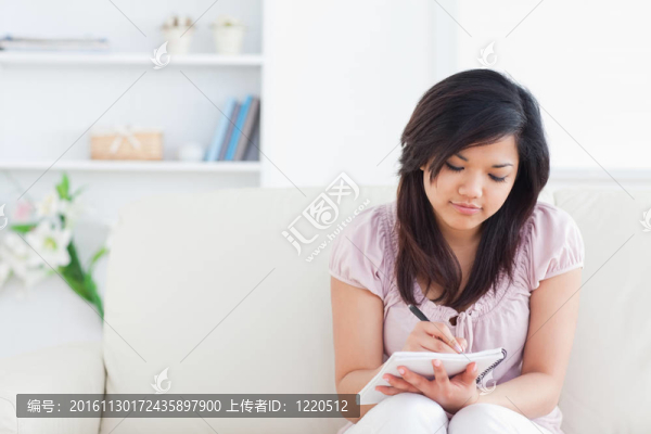 女人坐在沙發(fā)上，一邊在筆記本上寫(xiě)字
