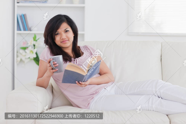 女人躺在沙發(fā)上，手里拿著一個杯子和一本書