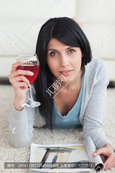 女人躺在地板上，拿著一杯酒和一個(gè)雜志