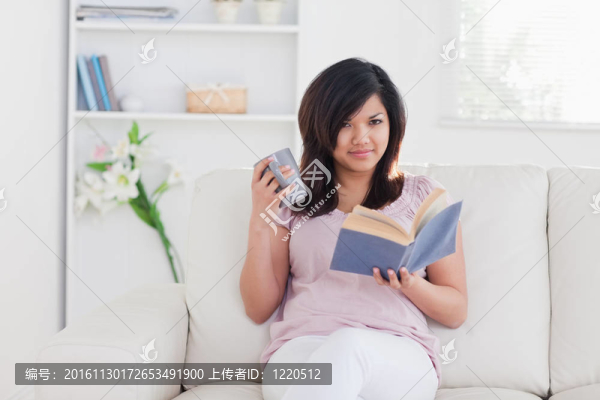 女人坐在沙發(fā)上，手里拿著一個杯子和一本書