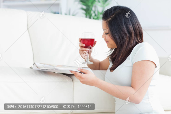 女人跪著看雜志，手里拿著一杯紅葡萄酒