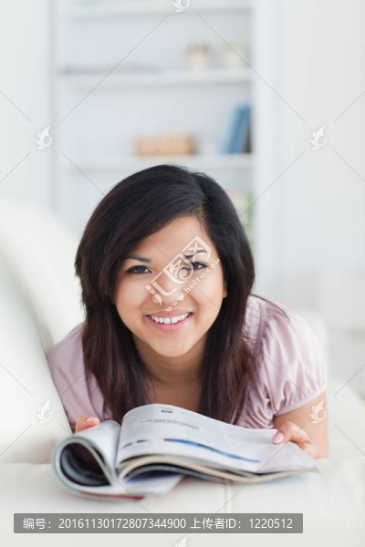 面帶微笑的女人躺在沙發(fā)上拿著一本雜志