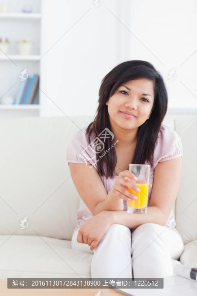 女人坐在沙發(fā)上捧著一杯橙汁