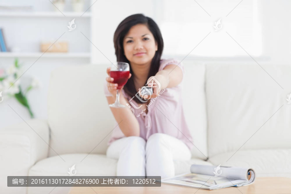 拿著電視遙控器和一杯紅酒的女人