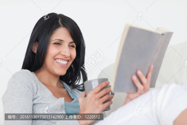女人拿著一個灰色的杯子和一本書微笑
