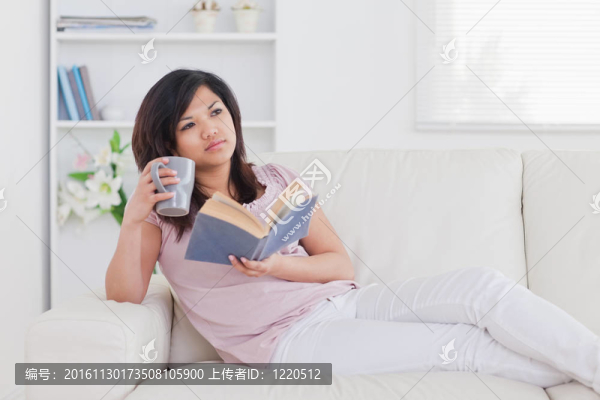 女人躺在沙發(fā)上，手里拿著一本書和一個(gè)杯子