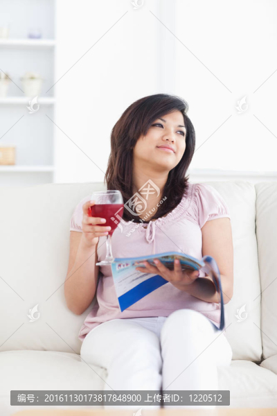 女人坐在沙發(fā)上，手里拿著一杯紅酒和一杯