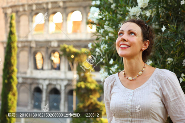 漂亮的年輕女人站在Colosseum上看；白色的花朵布什