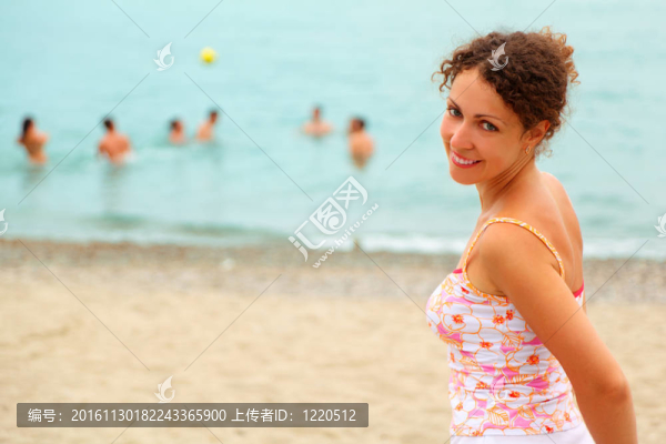 海灘上穿著粉紅色襯衫的漂亮女子；在海里玩球的人