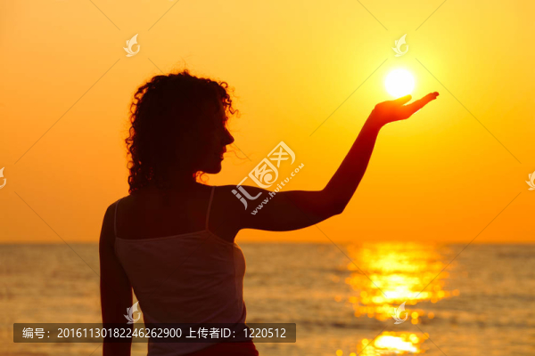 美麗的年輕女子站在海灘上；看日落；手牽著太陽