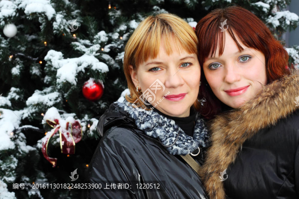 兩個(gè)女人站在綠樹近旁的雪里；媽媽和女兒