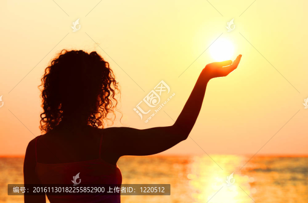 美麗的年輕女子站在海灘上；看日落；手牽著太陽