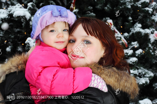 年輕女子與小微笑女兒站在綠樹附近與雪
